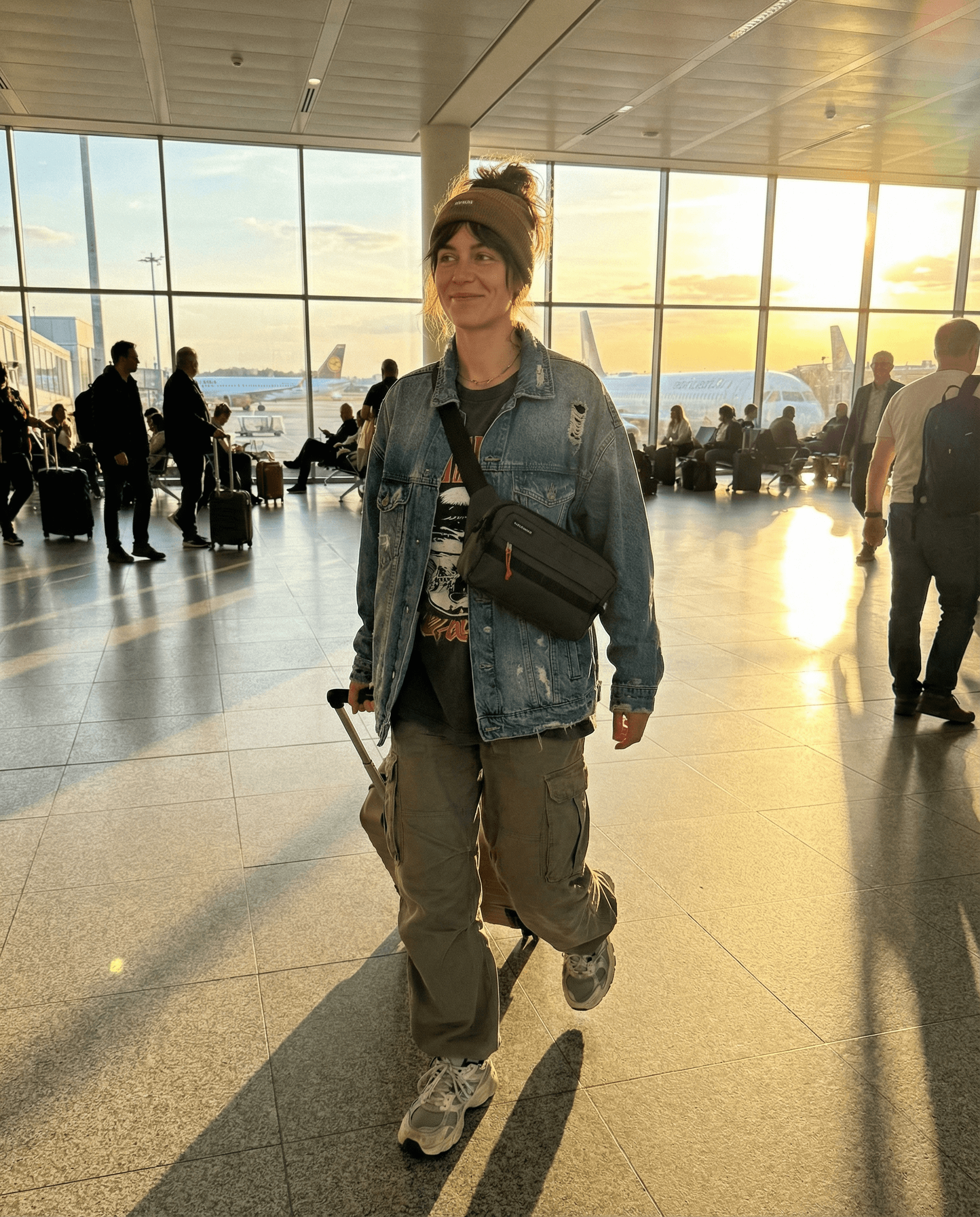 Cestující v letištní hale s nepromokavou crossbody ledvinka cordura KAI na rameni, sluneční světlo za ní.