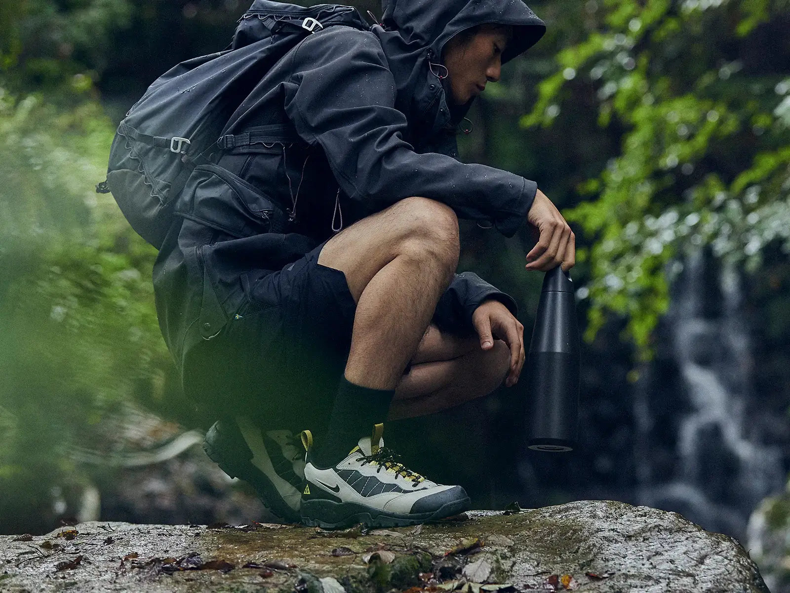 Man in outdoor gear holding a Trail Tumbler by a waterfall, showcasing nature and adventure.