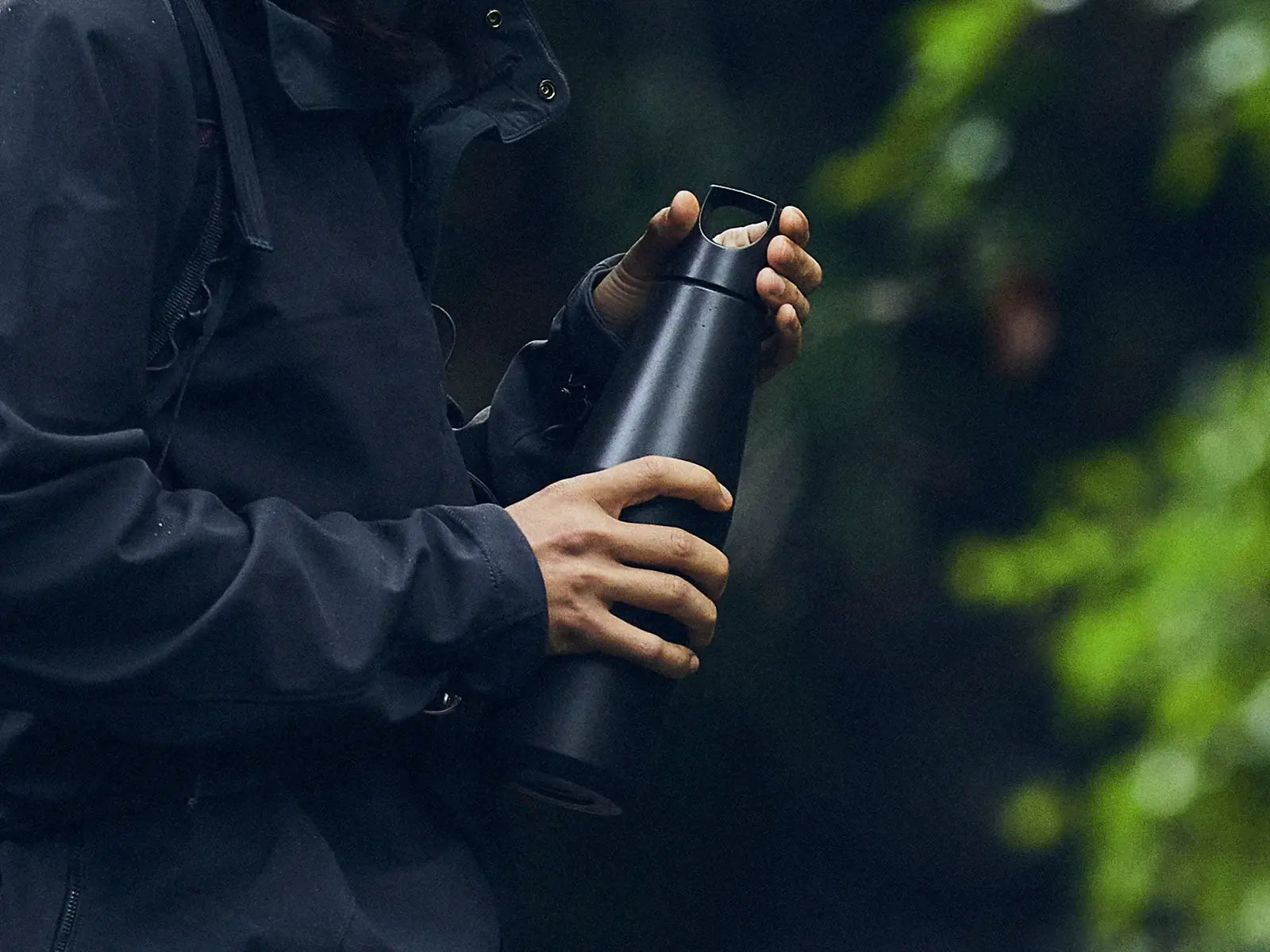 Person holding a black Trail Tumbler in a natural outdoor setting, perfect for hot or cold drinks.